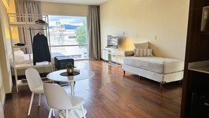 Une chambre d’hôtel moderne équipée d’un canapé, d’une table à manger avec des chaises, d’une télévision et d’un balcon offrant une vue sur la ville.