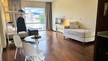 Una habitación de hotel moderna con sofá, una mesa de comedor con sillas, televisión y balcón con vistas a la ciudad.