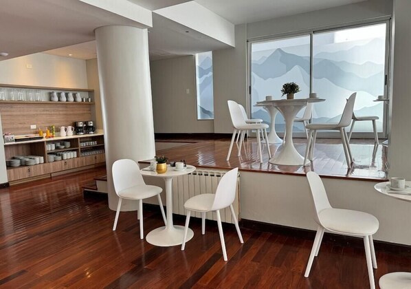 A modern interior with a wooden floor, white chairs, a round table, and a view of mountains through large windows.