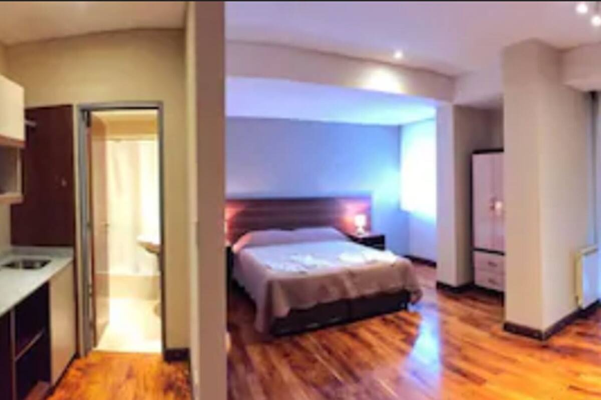 A hotel room with a wooden floor, a bed, a TV, and a bathroom with a shower and toilet.