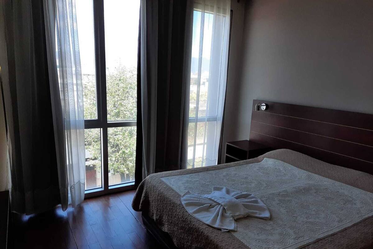 A hotel room with a large bed, a nightstand, and a window with curtains.
