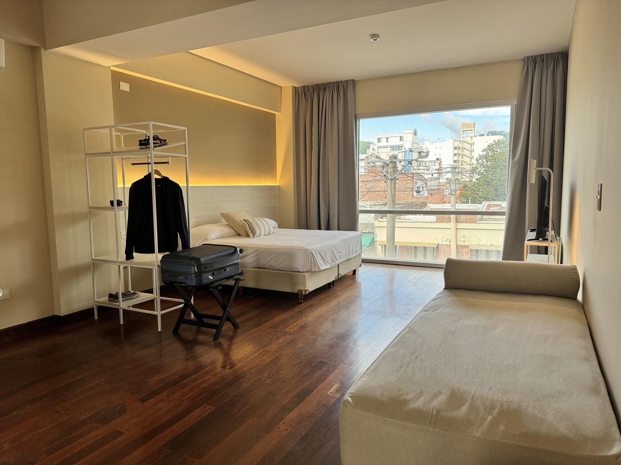 A hotel room with a bed, a seating area, a wardrobe, and a suitcase on a trolley.