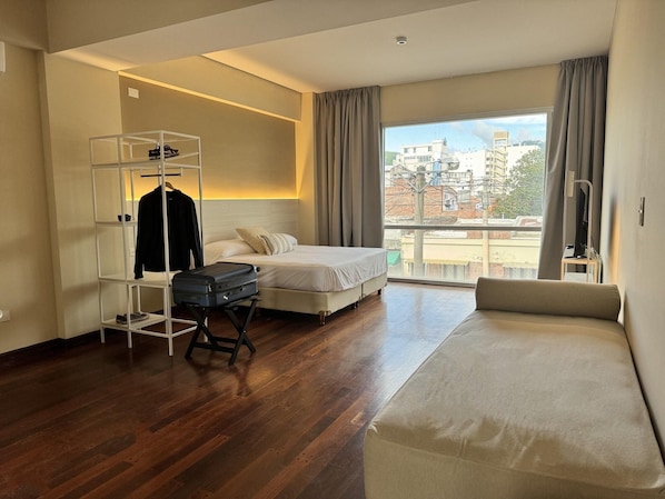 Quarto de hotel com cama, área de estar, guarda-roupa e mala em carrinho.