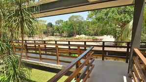 A covered outdoor area with wooden railings, a concrete floor, and a view of a natural landscape with trees and rocks. - Condo Sabia Apartments by CSR (Playa del Carmen)