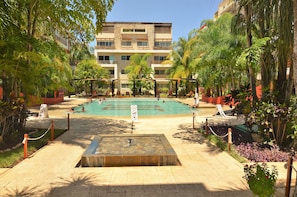 A pool area with a stone fountain, surrounded by palm trees and lounge chairs. - Condo Sabia Apartments by CSR (Playa del Carmen)