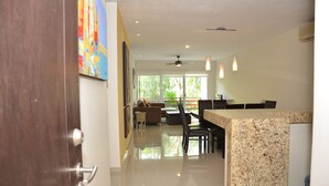 A modern kitchen with granite countertops, a dining area with a table and chairs, and a view of the outdoors through large windows. - Condo Sabia Apartments by CSR (Playa del Carmen)