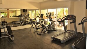 A gym with various exercise equipment, including treadmills and elliptical machines, and large windows offering a view of the outdoors. - Condo Sabia Apartments by CSR (Playa del Carmen)