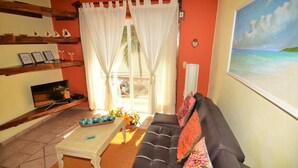A living room with a sofa, a coffee table, and a TV. There are curtains, a painting, and a shelf with decorative items. - Apartment Luna Antigua 2 BR 1 Bth (Playa del Carmen)
