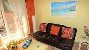 A living room with a black leather sofa, a wooden coffee table, and a painting of a beach scene on the wall. - Apartment Luna Antigua 2 BR 1 Bth (Playa del Carmen)