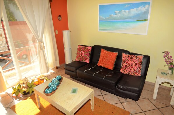 A living room with a black leather sofa, a wooden coffee table, and a painting of a beach scene on the wall.