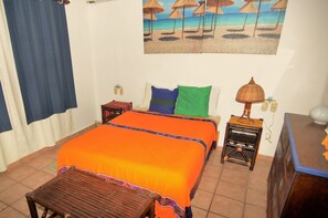 A bedroom with a bed, a nightstand, a lamp, and a painting of a beach scene. - Apartment Luna Antigua 2 BR 1 Bth (Playa del Carmen)