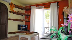 A living room with a television, wooden shelves, a sofa, and a window with curtains. - Apartment Luna Antigua 2 BR 1 Bth (Playa del Carmen)