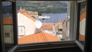 A view from a window overlooking a coastal town with terracotta-roofed buildings, a satellite dish, and a body of water with boats. - Apartments Neno (Korcula)