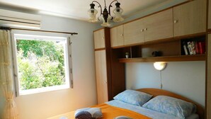 A bedroom with a bed, a window, a ceiling light, and a wooden wardrobe. - Apartments Neno (Korcula)