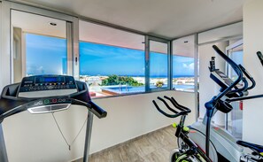 A modern gym with a treadmill, stationary bikes, and a view of the ocean. - Penthouse Skyline 2BR 2BathR & Balconies (Playa del Carmen)