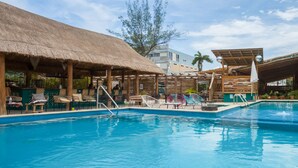 Una piscina con sillones de descanso y una estructura de techo de paja.