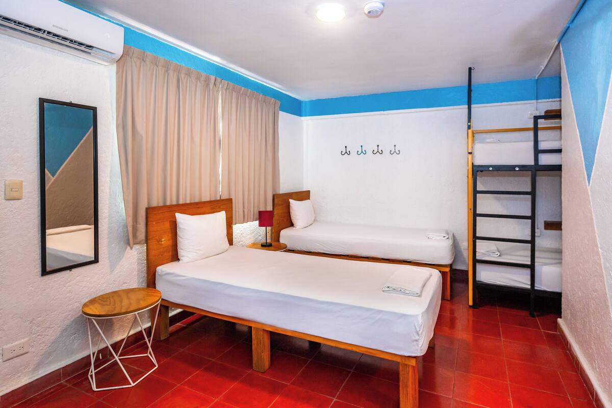 Ein Zimmer mit zwei Betten, einem Spiegel, einem kleinen Hocker und einer Regalwand.