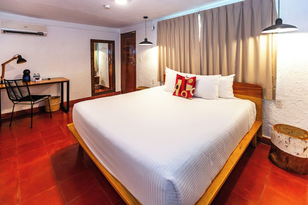 Ein Hotelzimmer mit einem großen Bett, einem Schreibtisch mit Stuhl, einem Spiegel und einem Vorhangfenster.