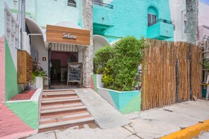 Um edifício com uma placa indicando "Selina" na entrada, uma escadaria que leva à porta e uma cerca de madeira na frente.