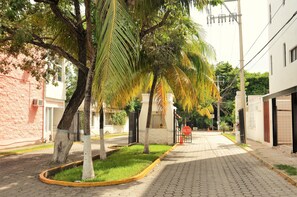 A paved street lined with palm trees and a building with a gated entrance. - Apartment 1 Bedroom Tohoku (Playa del Carmen)