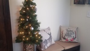En liten hörna med ett fint dekorerat julgran, en bänk med kuddar och en väggmonterad klädhängare.