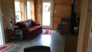 Ein Holzblockhaus im Inneren mit einem roten Sofa, einem Sessel, einem Kamin und einem Fernseher.