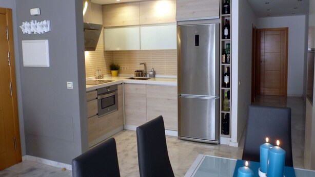 Een moderne keuken met een roestvrijstalen koelkast, houten kastjes en een ingebouwde wijnrek.
