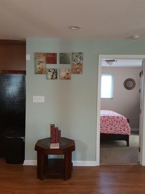 A room with a wooden floor, a table with books, a bed with a patterned bedspread, and a wall with motivational posters.