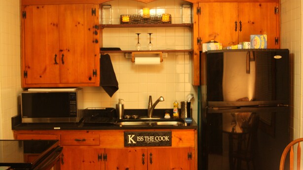 Una cocina con armarios de madera, un microondas de acero inoxidable, un fregadero y un refrigerador.