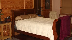 Un dormitorio con paneles de madera, una cama, una mesita de noche, una silla y una ventana con persianas.