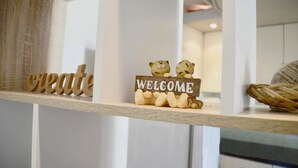 A wooden shelf with a 'create welcome' sign and two cat figurines. - King Deluxe Apartments (Melbourne)