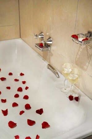 A bathtub with rose petals and two glasses of white wine. - King Deluxe Apartments (Melbourne)