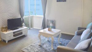 A living room with a sofa, a coffee table, a TV on a stand, and a window with curtains. - King Deluxe Apartments (Melbourne)