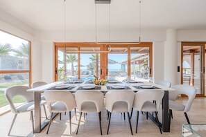 A modern dining area with a large table, multiple chairs, and a view of the sea. - Golden sand beachfront villa ,6 Bedrooms,Rethymno (Rethymno)