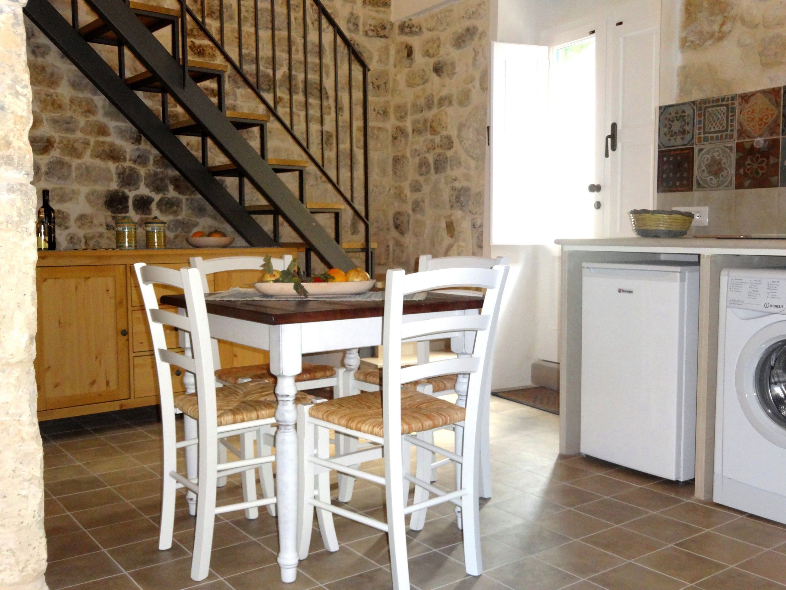 Una cucina con tavolo da pranzo, sedie, lavatrice e una scala.