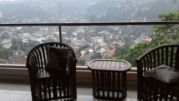 Un balcón con dos sillas de madera y una mesita pequeña, con vistas a un paisaje urbano que incluye edificios y colinas.
