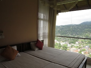 A hotel room with a bed, a window with a view of a city and mountains, and a curtain.