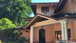 Una casa de dos pisos con piscina, un patio cubierto y un jardín.