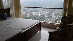 Un dormitorio con una cama, una silla y vistas a un paisaje urbano a través de amplios ventanales.