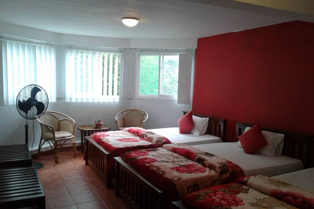 Une chambre avec deux lits, un ventilateur, une chaise et une petite table.