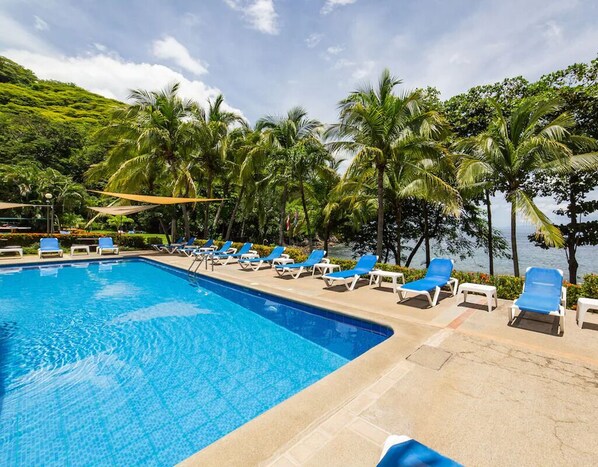 Una piscina con agua azul, rodeada de sillas de descanso y palmeras.