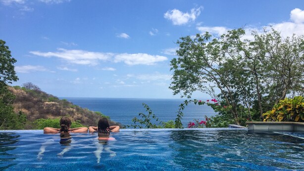 Una piscina con agua cristalina azul, rodeada de vegetación y con vistas panorámicas.