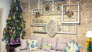 Una habitación acogedora con un árbol de Navidad, un sofá con cojines florales y una pared de ladrillo con la palabra "NOLA" sobre una vitrina.