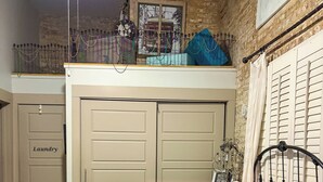 Un dormitorio con cama, armario, balcón y vistas a la calle a través de una ventana.