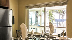 A dining area with a view of a balcony, a refrigerator, and a dining table set with plates and glasses. - Luxury Ocean View, Across from the Beach #5 (Carlsbad)