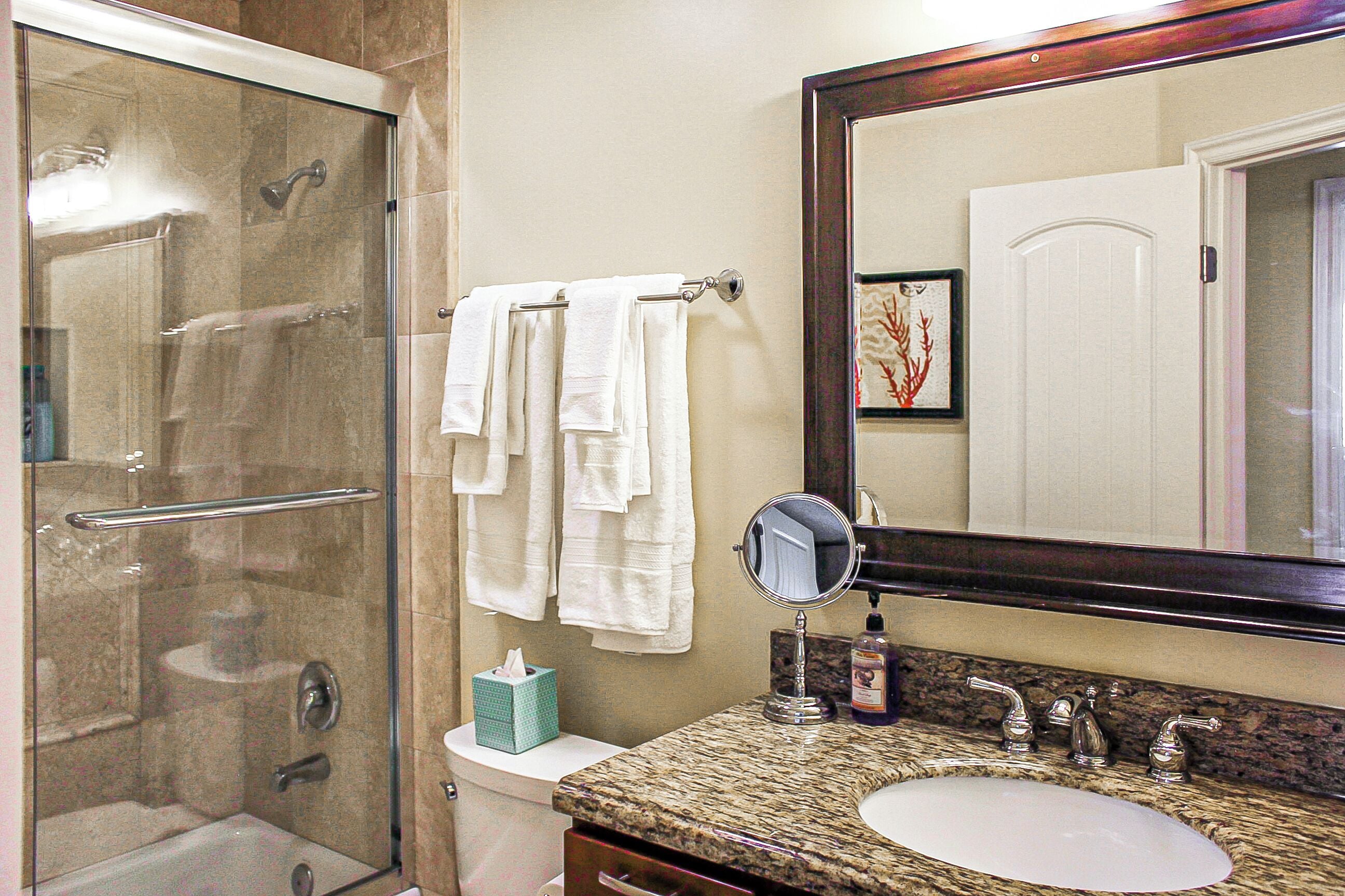 A bathroom with a glass-enclosed shower, a sink with a marble countertop, and a large mirror.