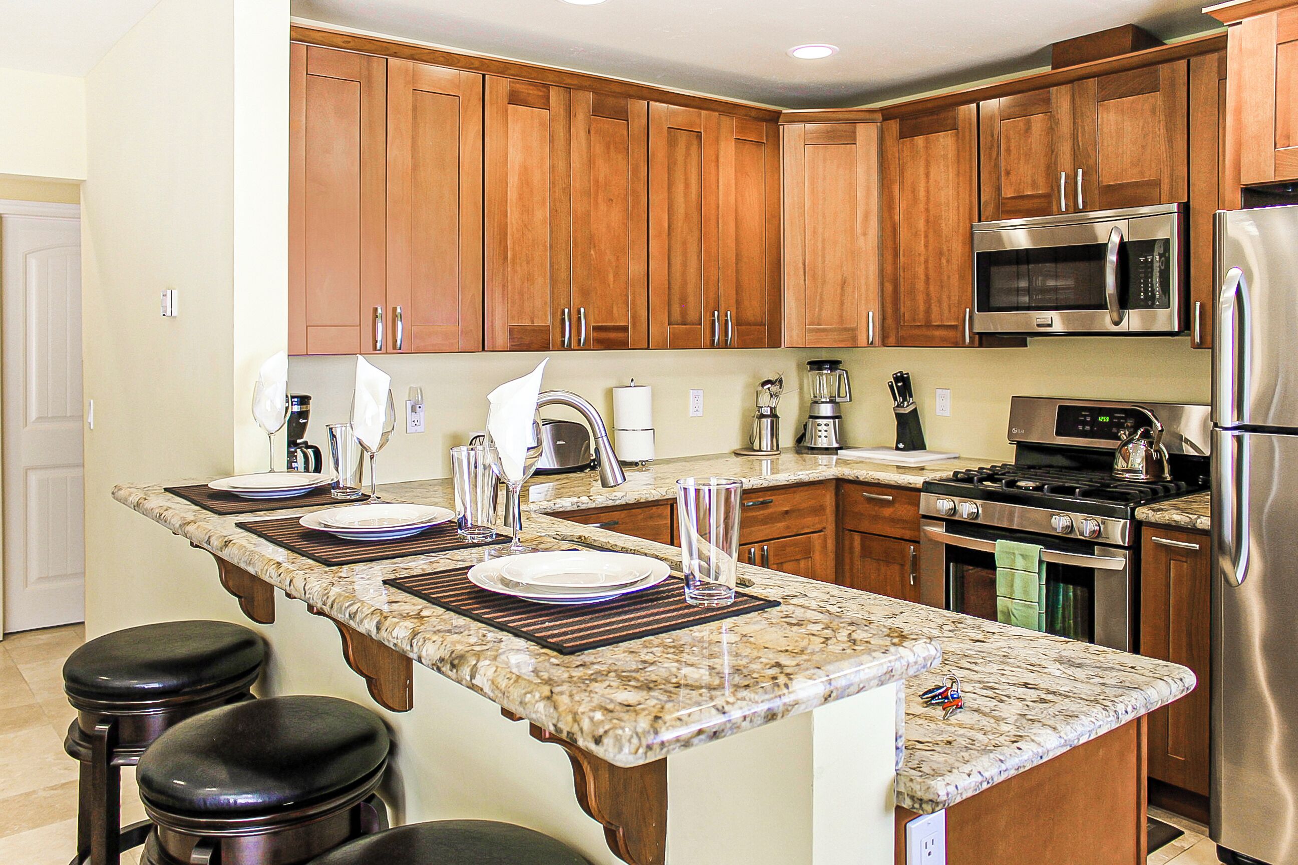 A kitchen with wooden cabinets, a stainless steel refrigerator, a microwave, and a stove.