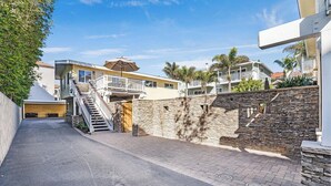 A residential street with a two-story house featuring a stone wall, a wooden door, and a staircase leading to a balcony. - Luxury Ocean View, Across from the Beach #5 (Carlsbad)