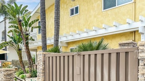 A gated residential area with a yellow house, palm trees, and a stone wall. - Luxury Ocean View, Across from the Beach #5 (Carlsbad)