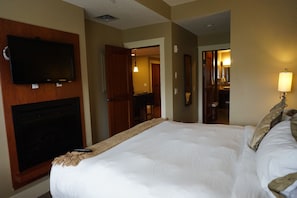 A hotel room with a large bed, a flat-screen TV mounted on the wall, a fireplace, and a mirror. - Relaxing Suite in 5 star resort ski, hike, dine, relax ! (Canmore)